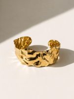 Pulseira rígida aberta em aço dourado com formas orgânicas e superfície irregular brilhante
