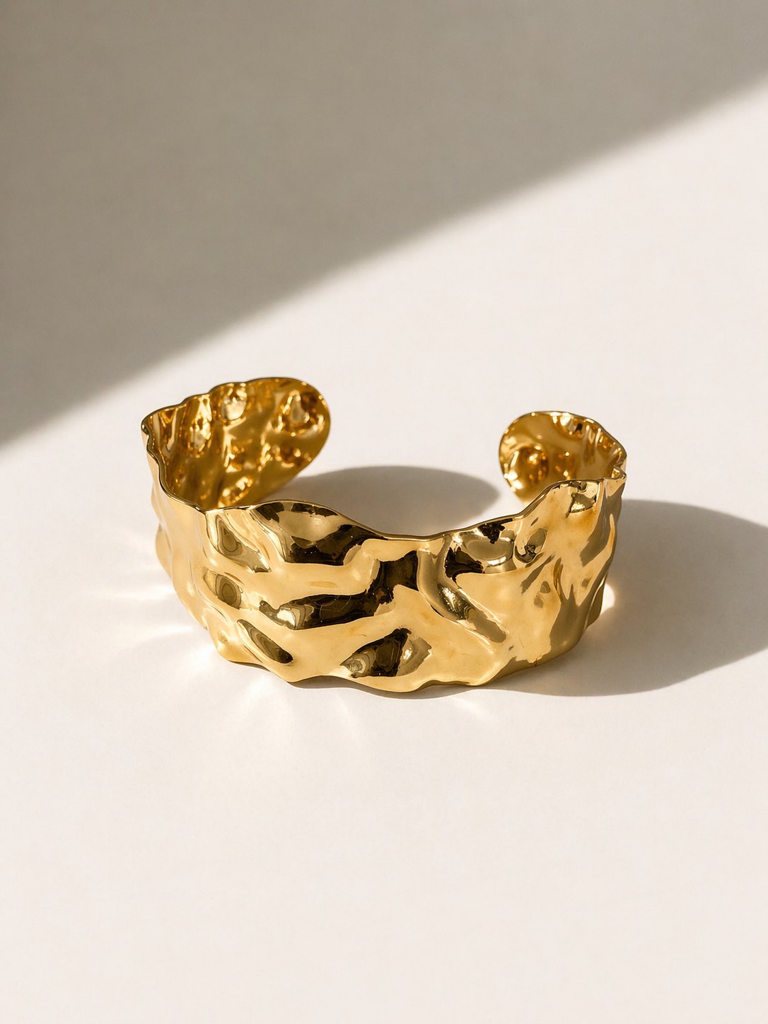 37922989-7dcf-4b52-87f8-5138b1d44828 Pulseira rígida aberta em aço dourado com formas orgânicas e superfície irregular brilhante