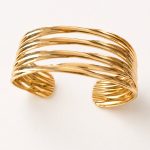 Pulseira rígida aberta em aço dourado com vários aros curvos entrelaçados e acabamento brilhante