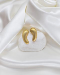 Brincos dourados em forma de gota sobre tecido branco