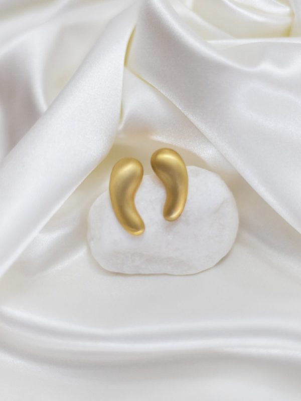 Brincos dourados em forma de gota sobre tecido branco