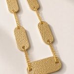 Colar em aço dourado com placas retangulares texturizadas ligadas por corrente de elos