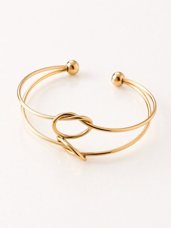 Pulseira rígida aberta em aço dourado com aros duplos, nó central e extremidades com pequenas esferas