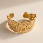 Pulseira rígida larga em aço dourado com elementos geométricos sobrepostos e textura em relevo