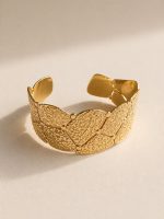 Pulseira rígida larga em aço dourado com elementos geométricos sobrepostos e textura em relevo