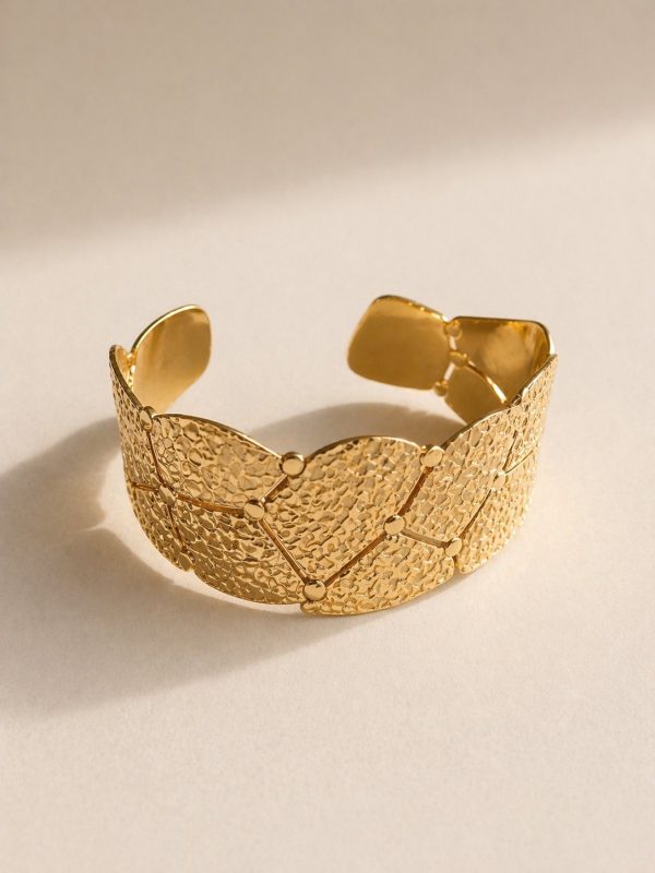 Pulseira rígida larga em aço dourado com elementos geométricos sobrepostos e textura em relevo