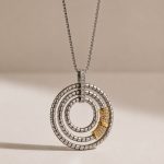 Colar circular em aço com aros concêntricos, detalhes dourados e pequenas pedras brilhantes