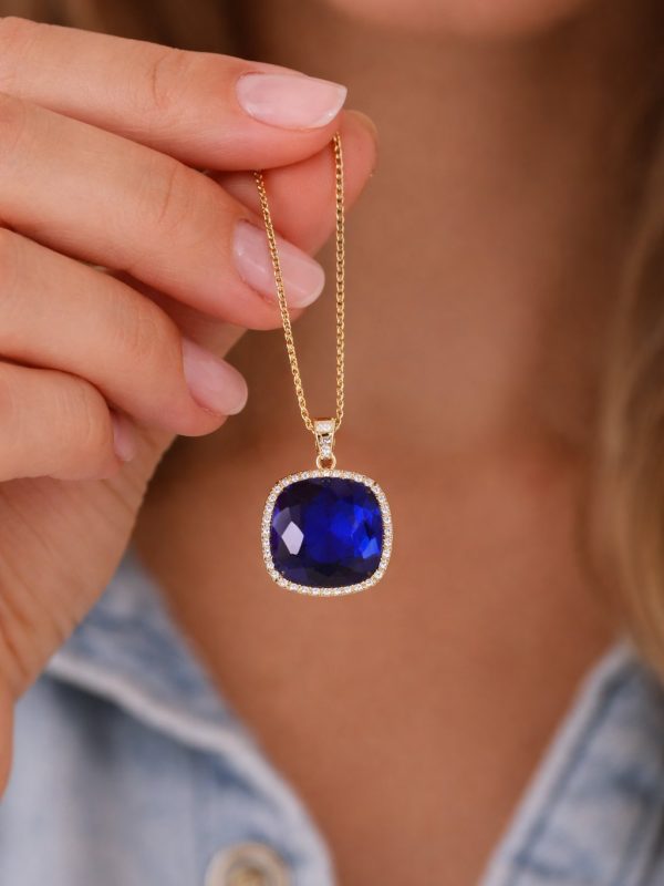 Colar em aço dourado com pedra azul intensa facetada e contorno de pequenas pedras brilhantes